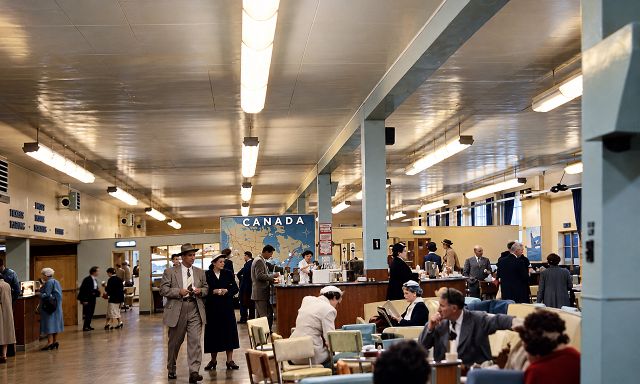 A busy terminal lounge with passengers seated and standing, and a large map of Canada on the far wall