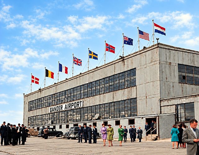 The Gander Airport terminal building seen from the side, flags flying on the roof and passengers on the apron